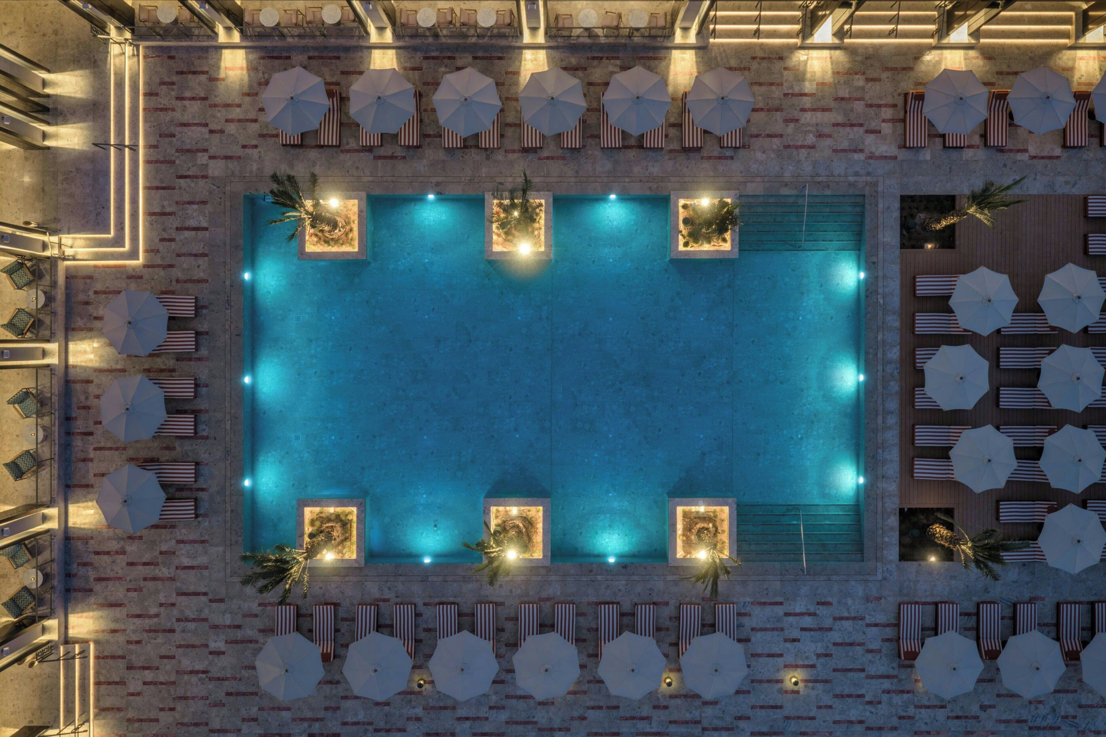 Ein Pool auf dem Dach mit Liegestühlen und Sonnenschirmen, umgeben von einer Ziegelmauer.
