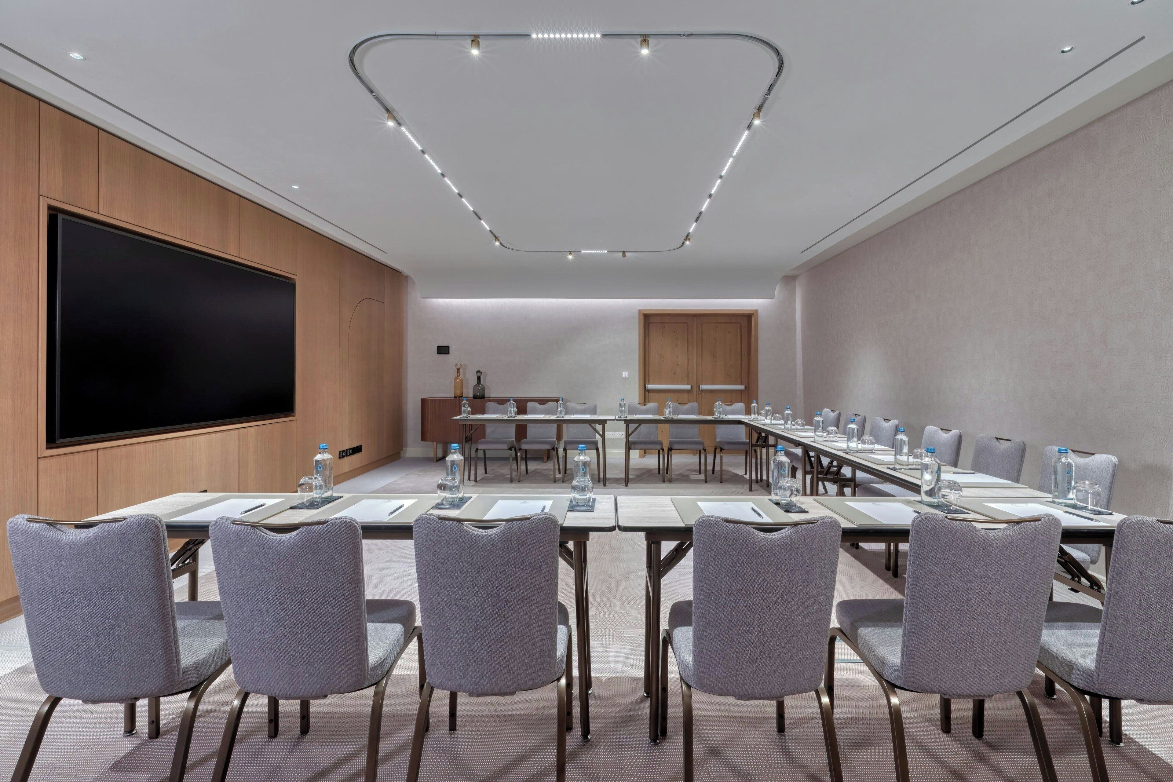 A conference room with a long table, chairs, a large screen, and a wooden cabinet.