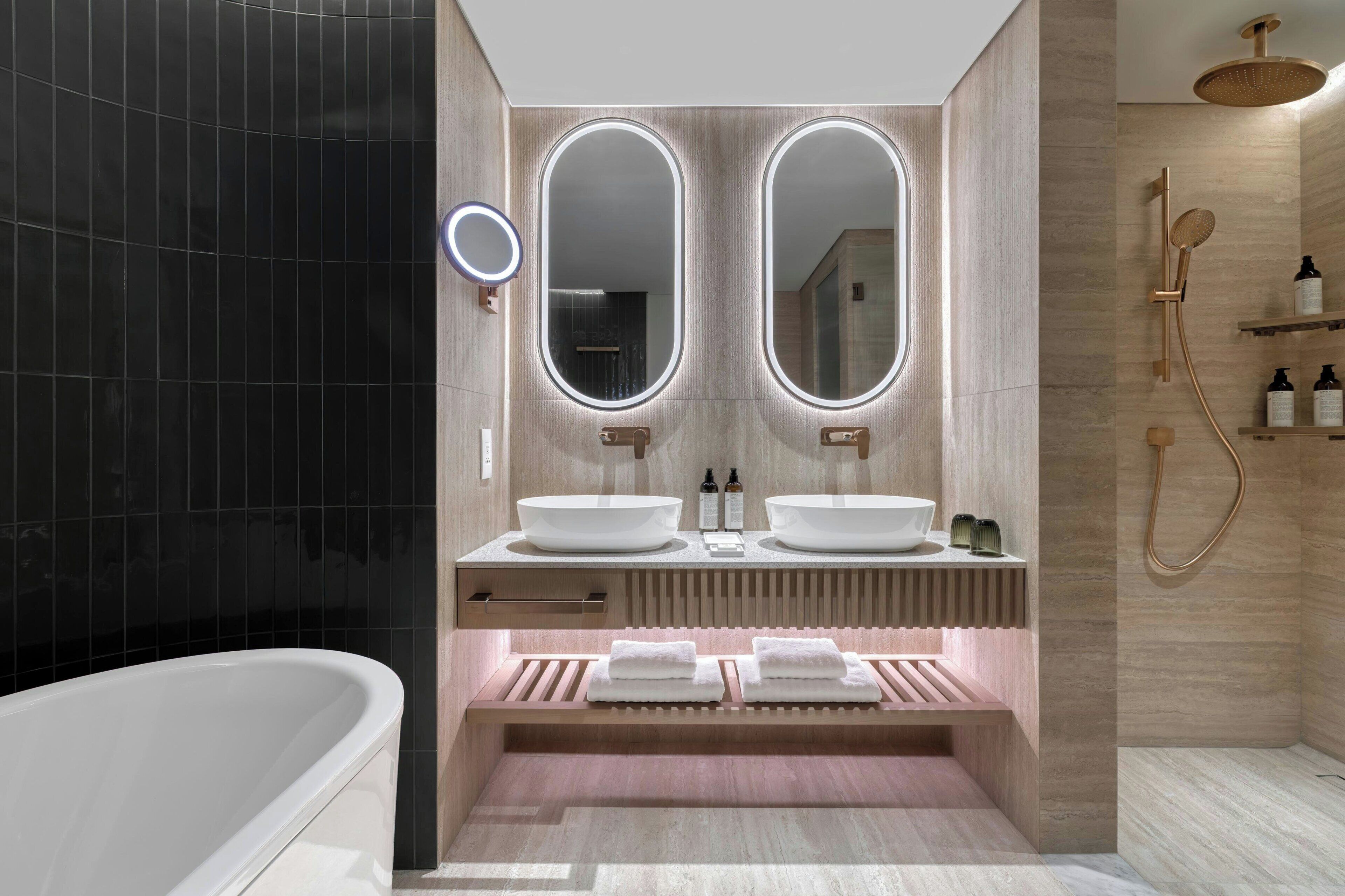 A modern bathroom with two sinks, a bathtub, and a shower area.