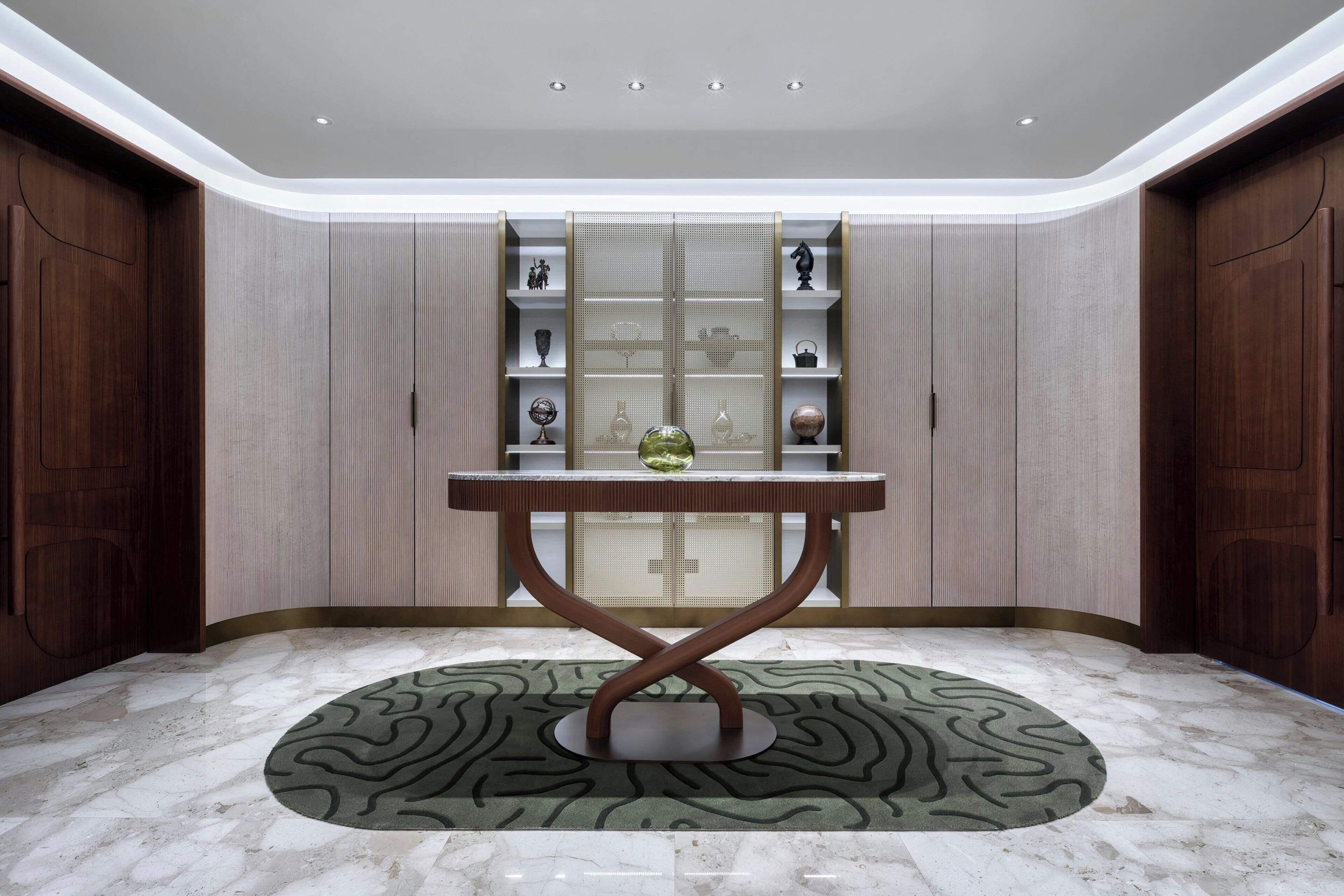 A room with a marble floor, a central table with a green patterned rug, and a shelving unit with decorative items.