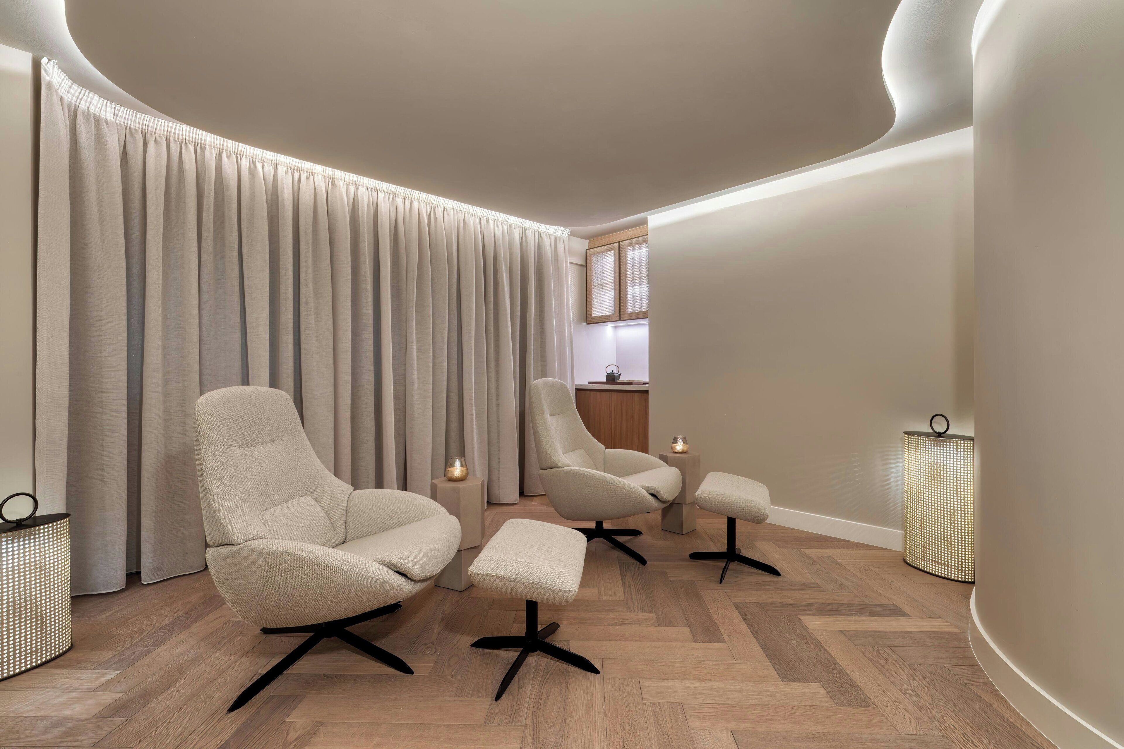 A modern living room with three chairs, a small ottoman, and a large window with curtains.