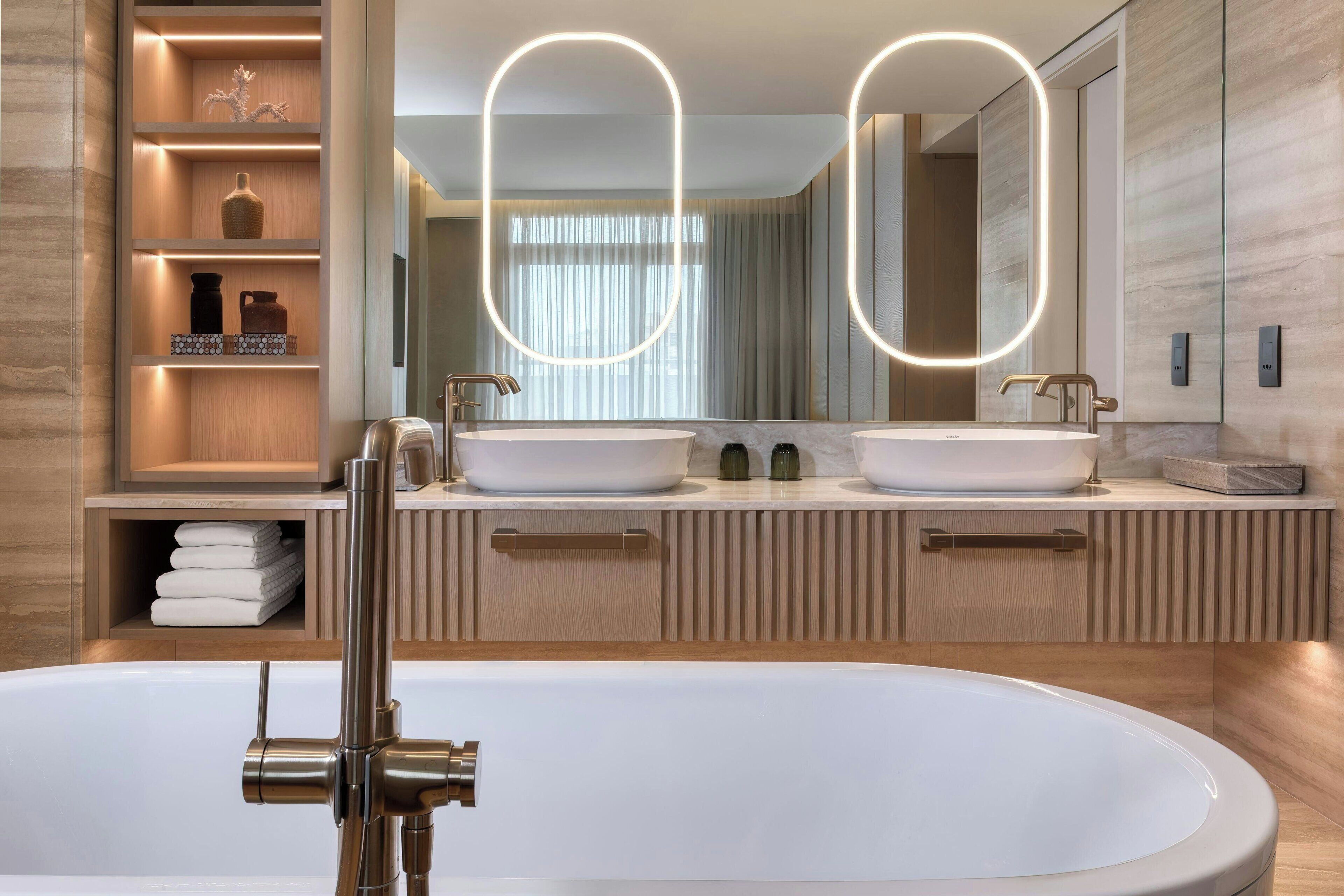 A modern bathroom with a freestanding bathtub, two sinks, and a vanity with a mirror.