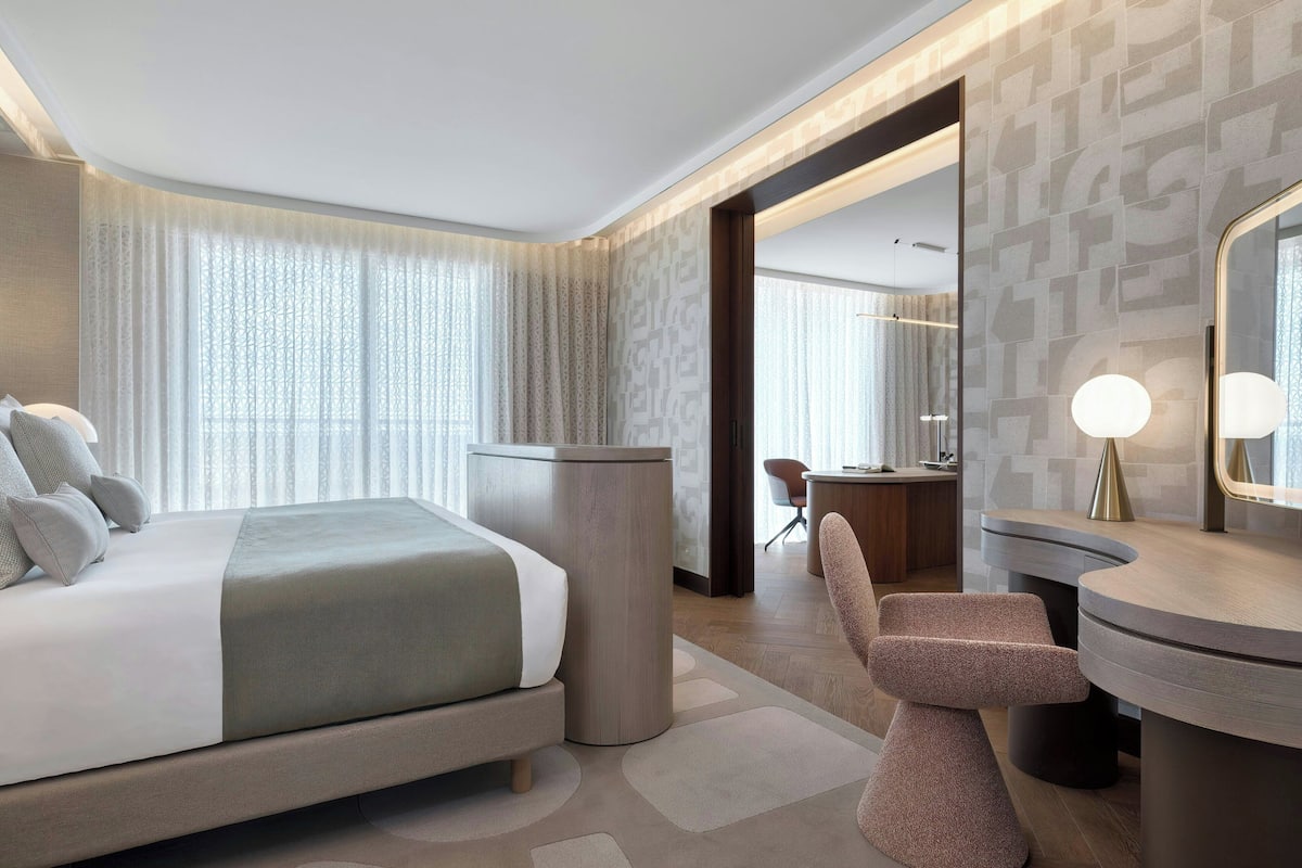 Ein modernes Hotelzimmer mit einem großen Bett, einem Schreibtisch, einem Stuhl und einem durch eine geöffnete Tür einsehbaren Badezimmer.