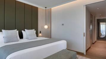 Une chambre d’hôtel moderne avec un grand lit, une table de chevet, un luminaire suspendu et une vue sur le couloir.