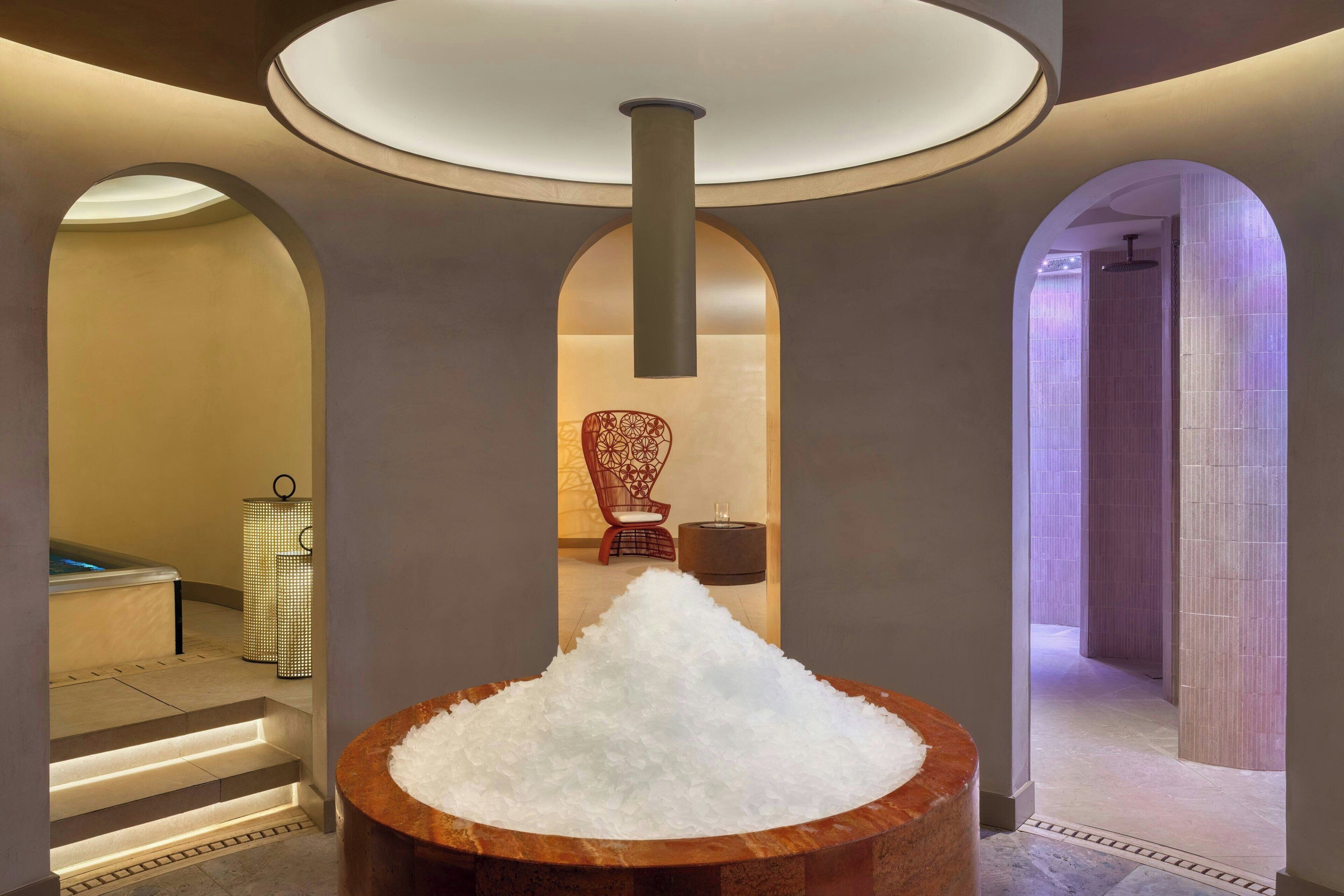 Un espacio de spa con un montón grande de piedras blancas, un banco de madera y una silla.