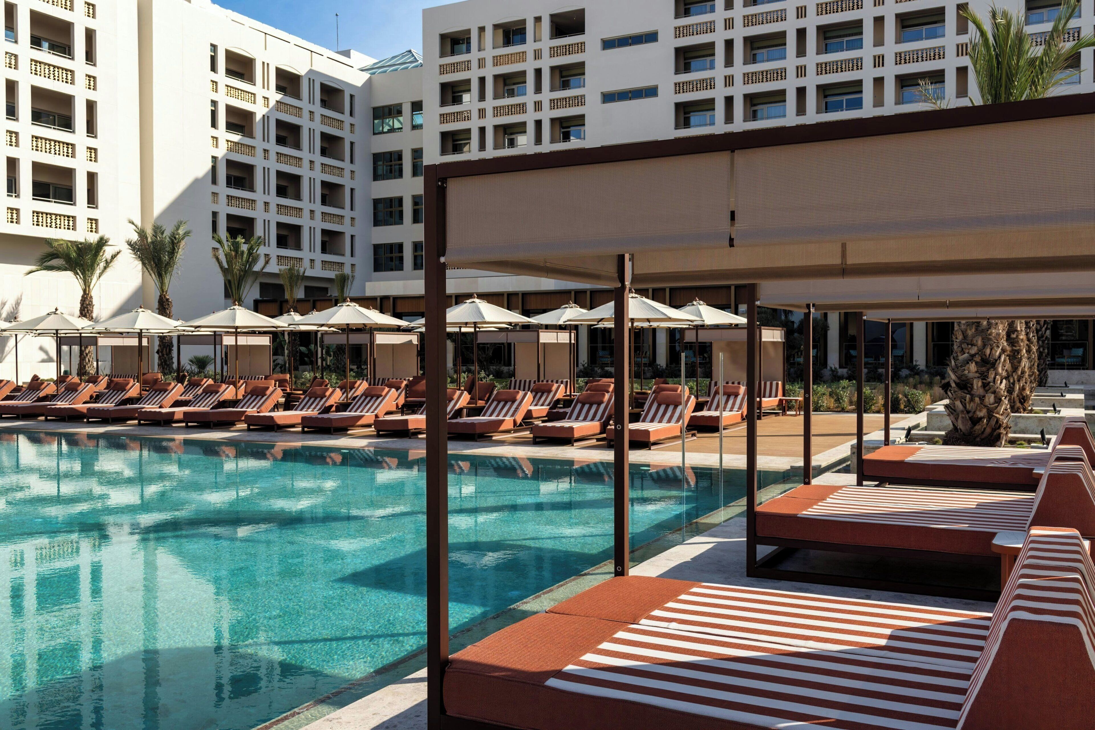 A pool area with lounge chairs and umbrellas, surrounded by a building with multiple balconies.