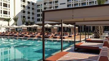 A pool area with lounge chairs and umbrellas, surrounded by a building with multiple balconies.