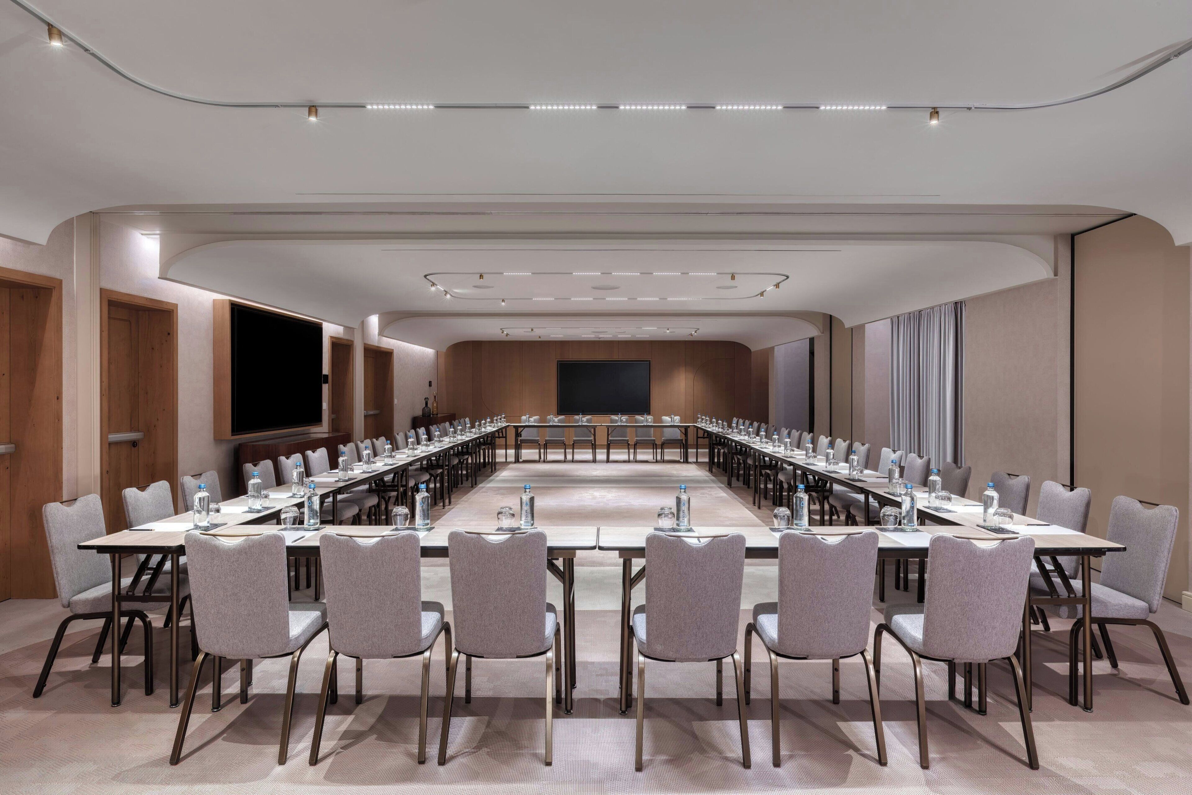 A conference room with a long table, multiple chairs, and a flat-screen TV.