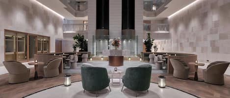 A modern lobby with seating areas, a central decorative piece, and a high ceiling with balconies.