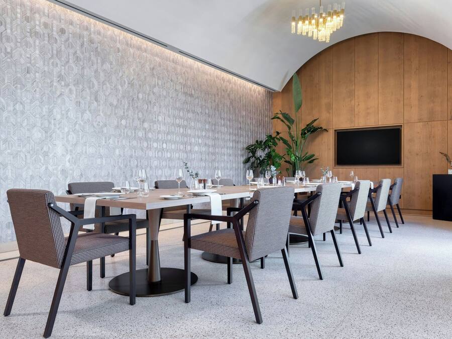 Un salón de conferencias con una larga mesa, sillas, una planta y una pantalla de televisión.