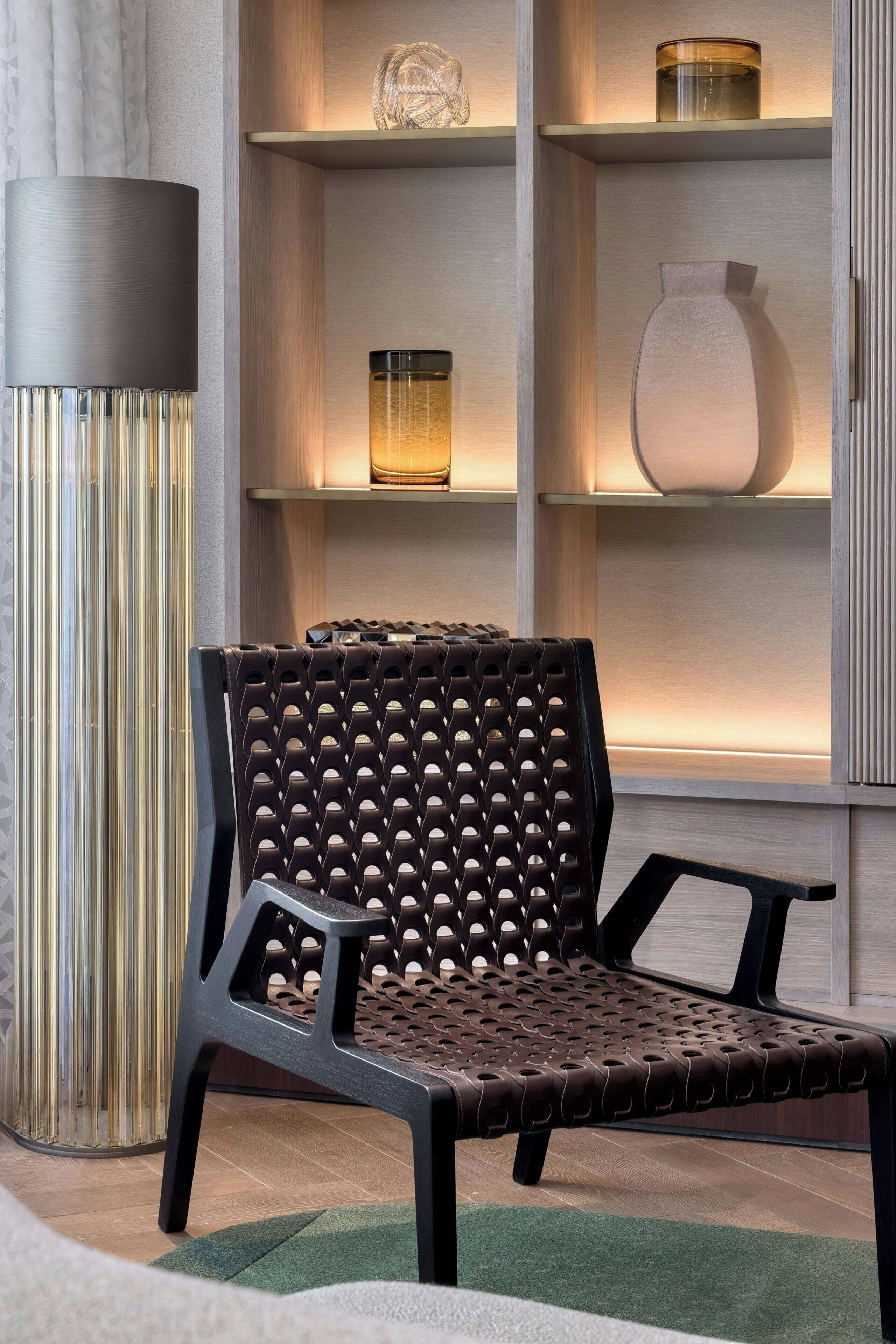 Un espace de détente moderne comprenant un fauteuil à haut dossier, un grand lampadaire et une étagère ornée d’objets décoratifs.