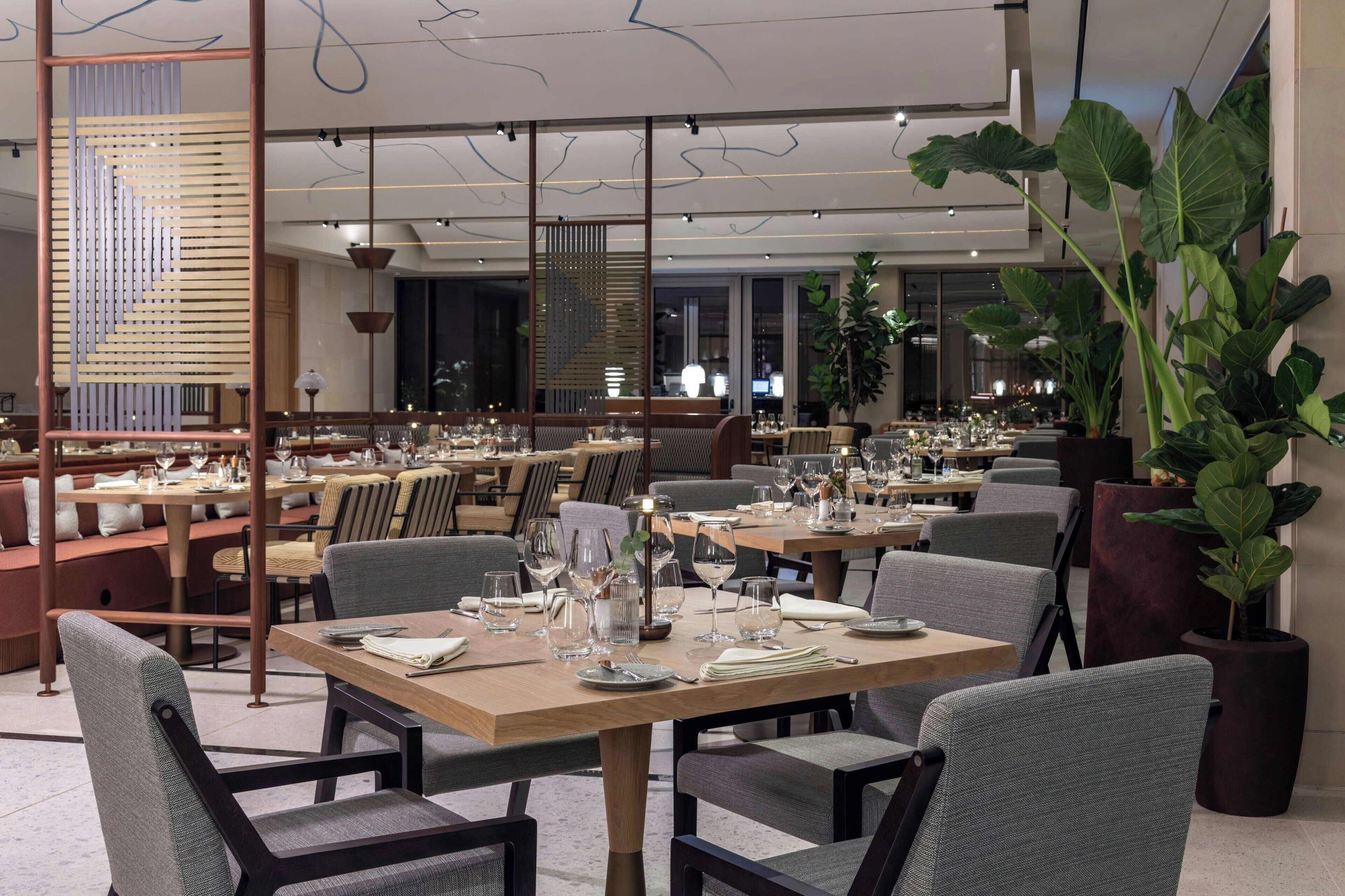 Un restaurante con varias mesas, sillas y plantas en macetas.