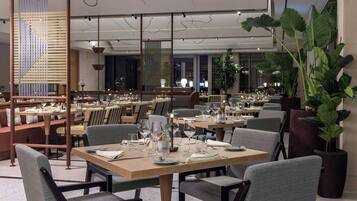 Un restaurante con varias mesas, sillas y plantas en macetas.