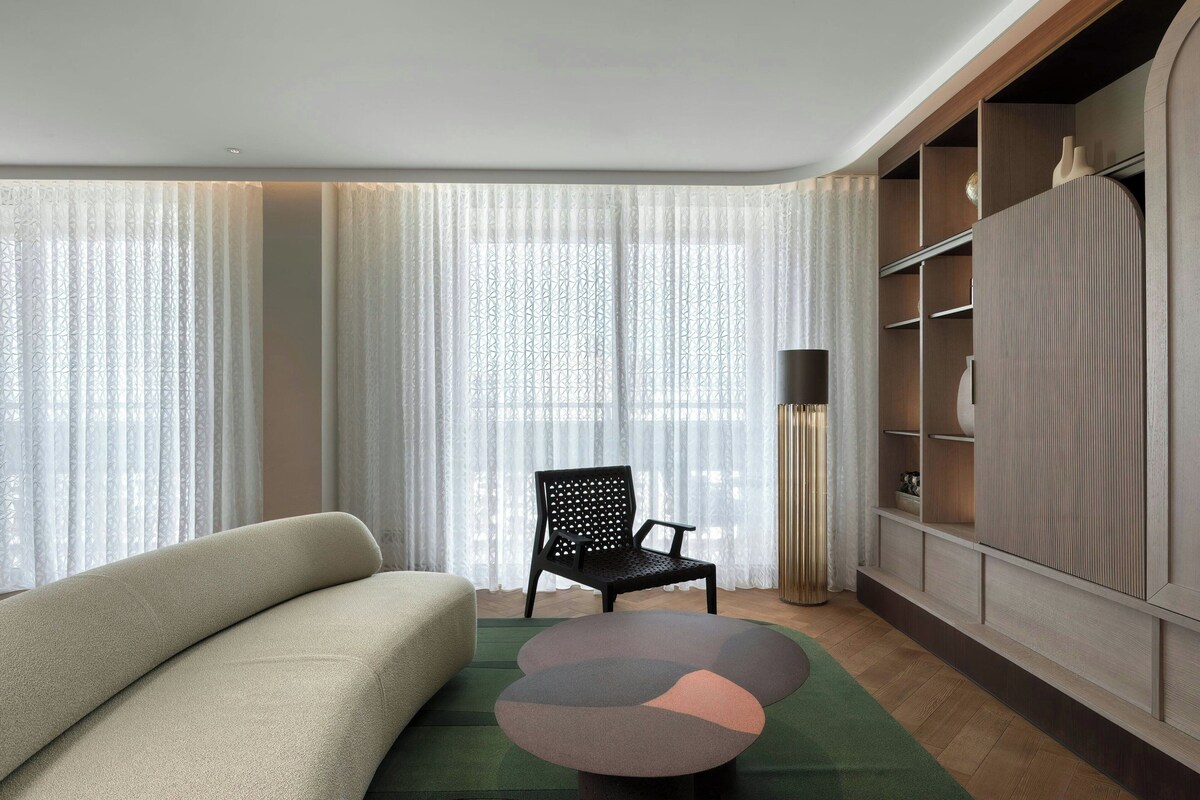 A modern living room with a sofa, a chair, a round table, and a built-in shelving unit.