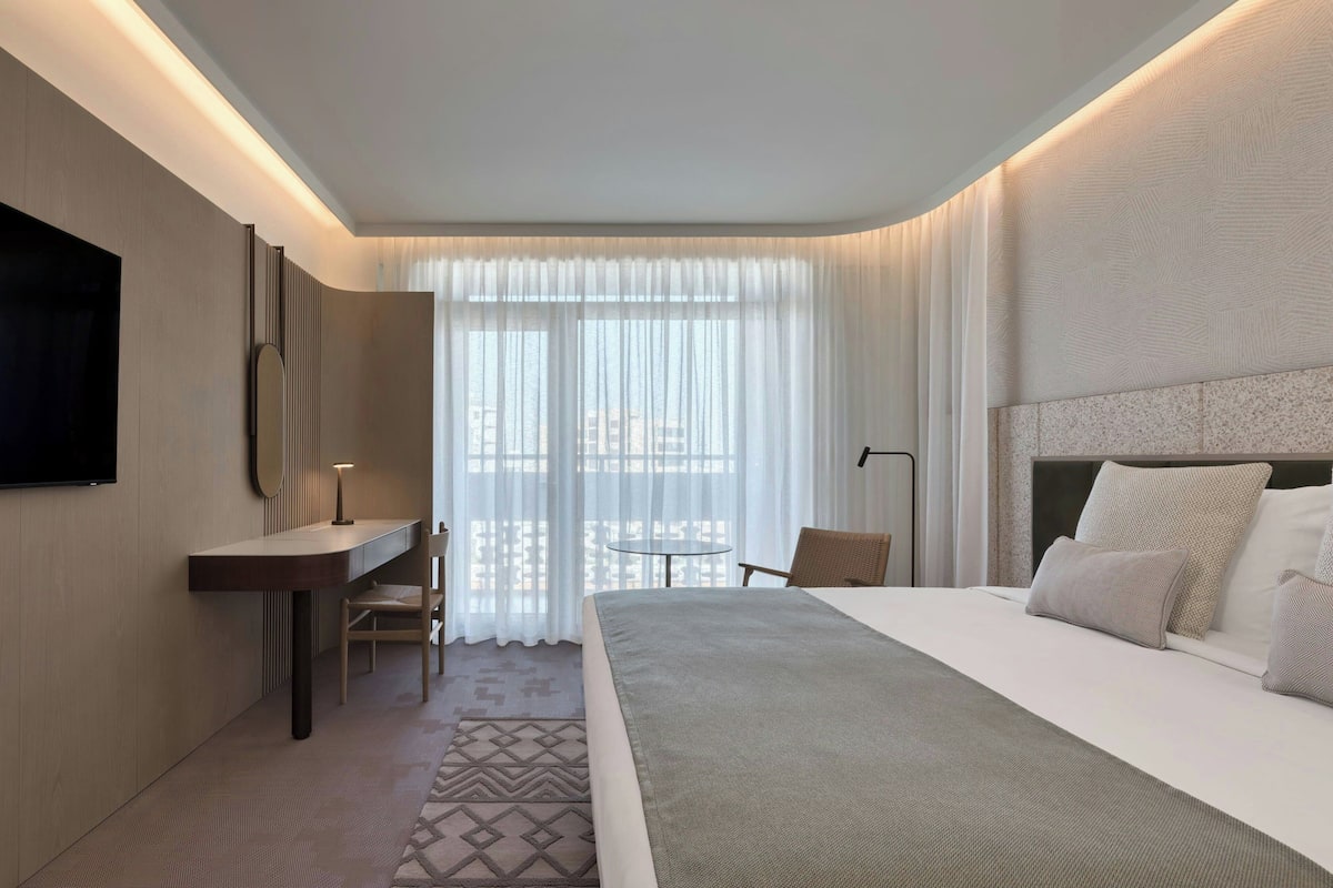 Et moderne hotelværelse med en stor seng, et skrivebord, en stol og et fjernsyn.