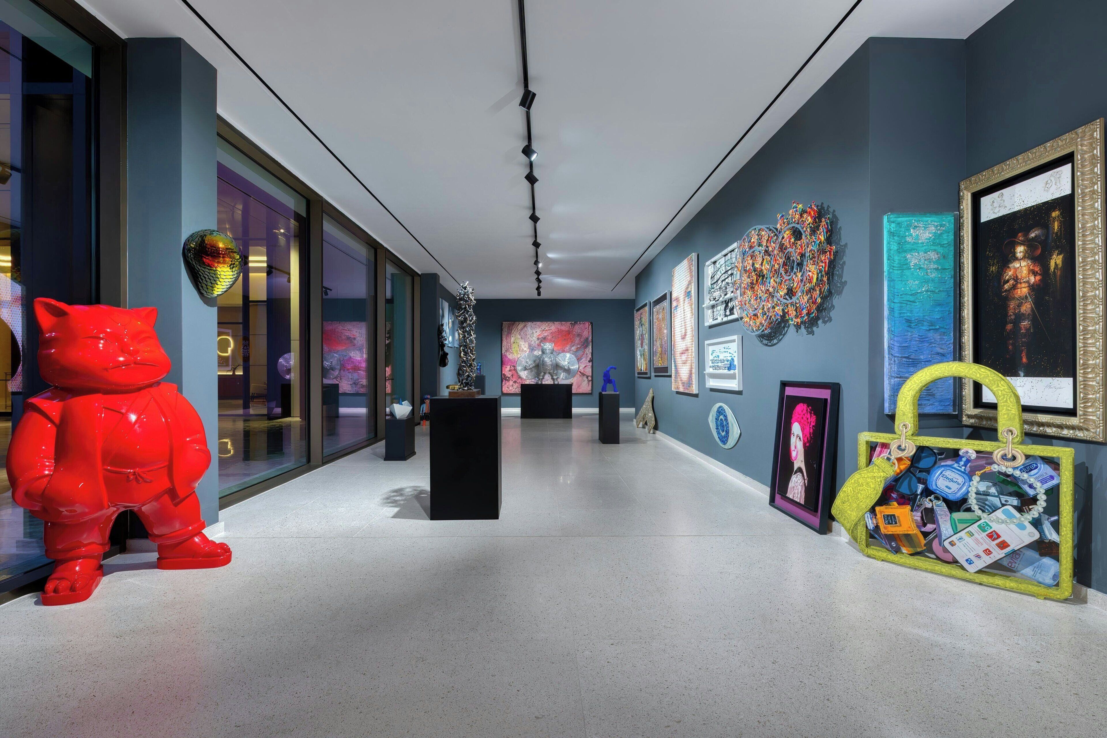 A modern art gallery with a red cat sculpture, abstract paintings, and a variety of displayed artworks.