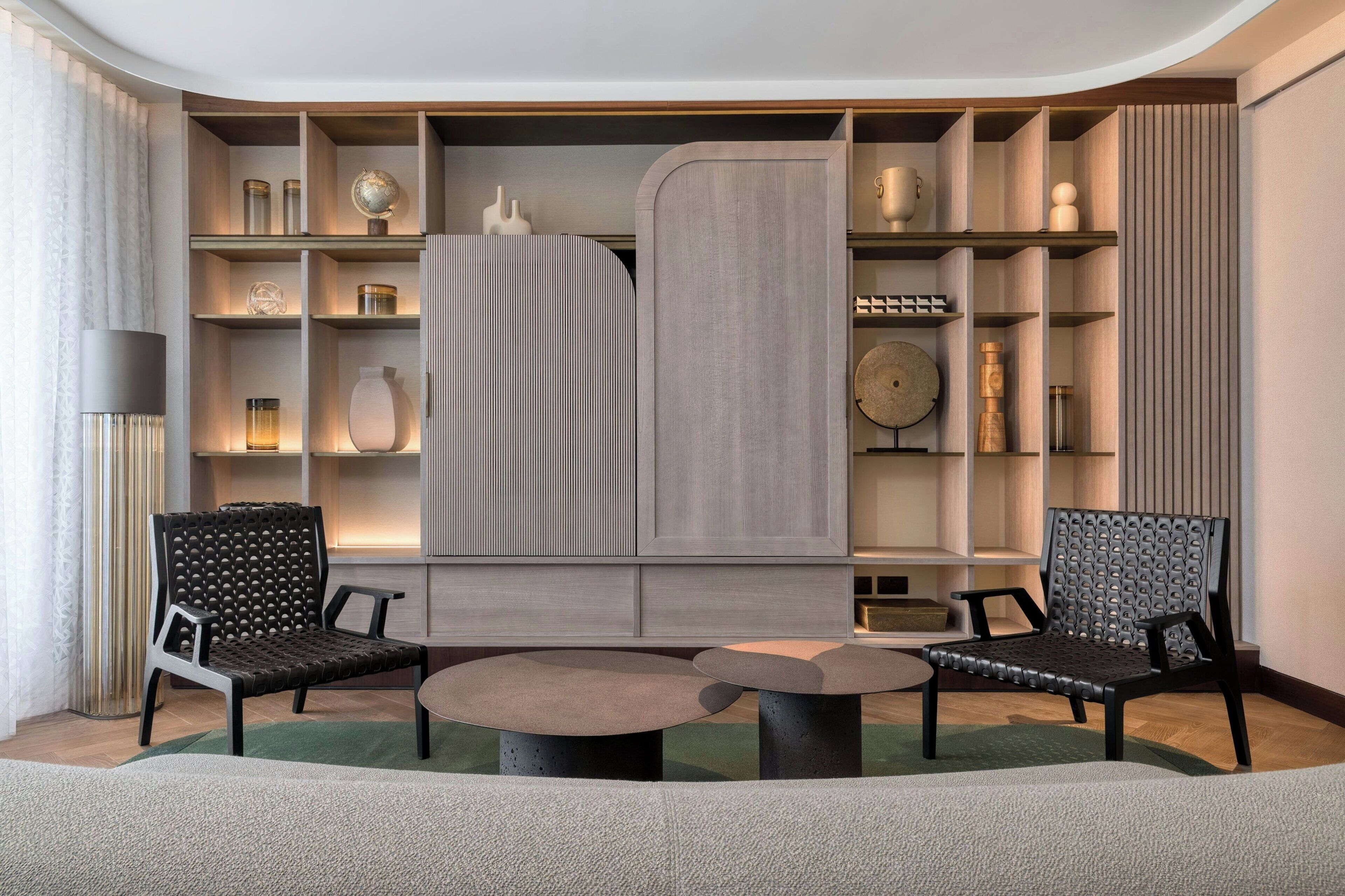 Una sala de estar moderna con dos sillas negras, una mesa redonda y una estantería empotrada con varios objetos decorativos.