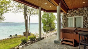 A covered outdoor area with stone flooring, a stone wall, and a view of a lake. - Lakefront Torch Lake Lodge  - 4 Floors of Luxury, 8 Bedrooms, Private Dock (Kewadin)