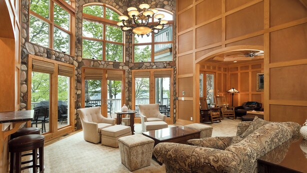 A spacious living area with large windows, stone walls, and wooden paneling. - Lakefront Torch Lake Lodge  - 4 Floors of Luxury, 8 Bedrooms, Private Dock (Kewadin)