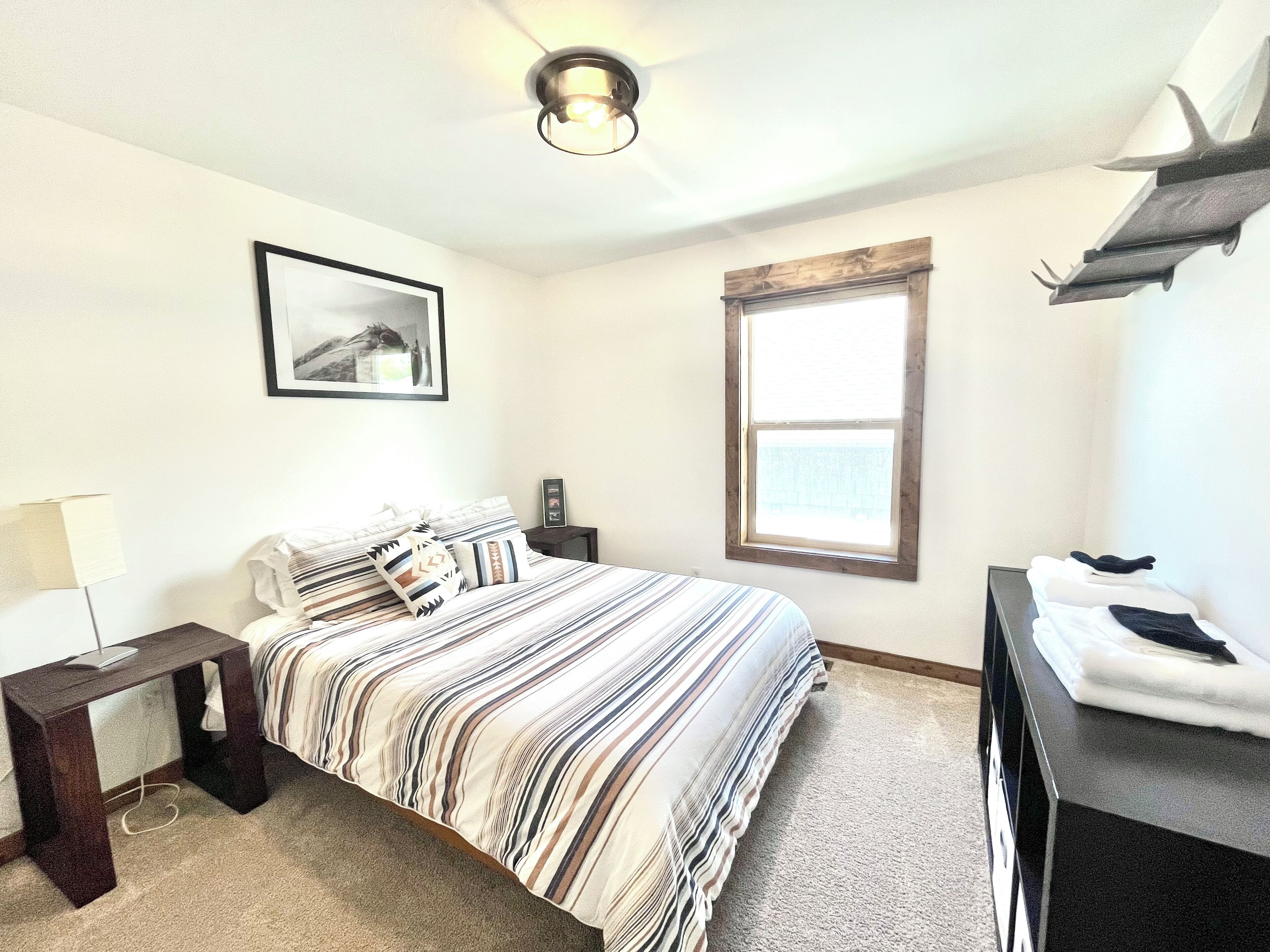 A bedroom with a bed, a nightstand, a lamp, a window, and a framed picture on the wall.