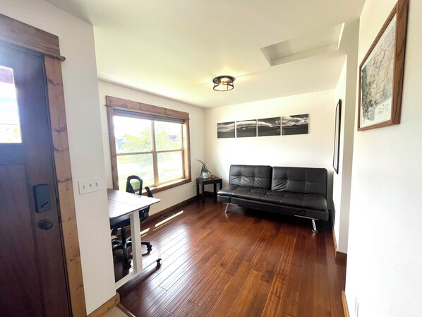 A living room with a black leather sofa, a wooden dining table with chairs, a large window with blinds, and a ceiling light fixture. - Beautiful Bozeman Home (Bozeman)