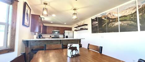 A modern kitchen with wooden cabinets, a central island, and a dining area with a wooden table and chairs.
