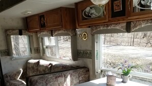 Interior de una caravana compacta con zona de comedor, asientos y una ventana que ofrece vistas a un paisaje rural.