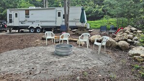 Un área recreativa con una caravana, una mesa de picnic, sillas y un pozo para fuego.