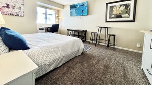 Une chambre d’hôtel avec un lit, un bureau, une chaise, une petite table et un tableau au mur.