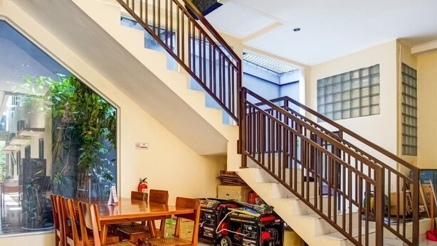 A spacious living area with a staircase, a dining table with chairs, and a large window overlooking a garden. - OYO 90037 Rumah Verde (Bogor)