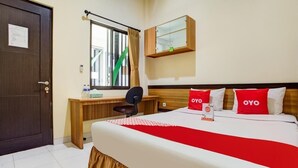 A hotel room with a wooden desk, a bed with red pillows, and a window with curtains. - OYO 90037 Rumah Verde (Bogor)