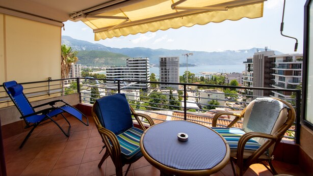 Un balcon avec des chaises bleues, une table ronde et un auvent jaune.