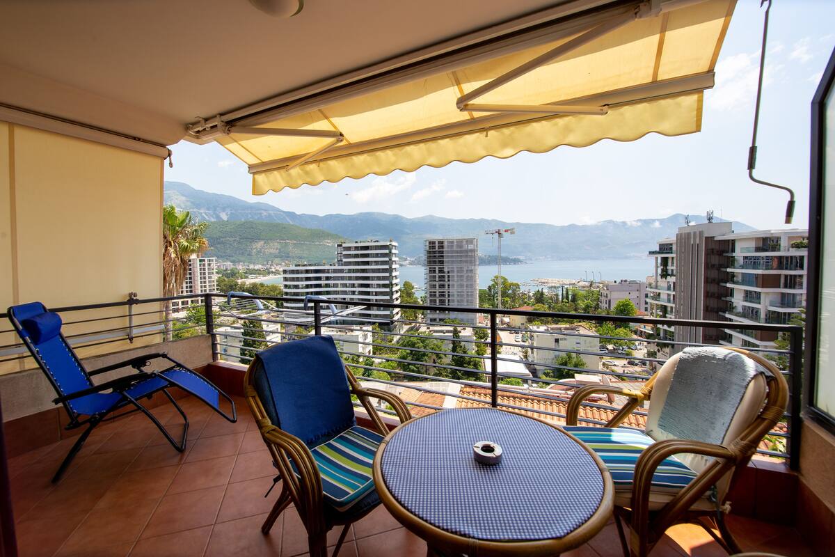 A balcony with blue chairs, a round table, and a yellow awning.