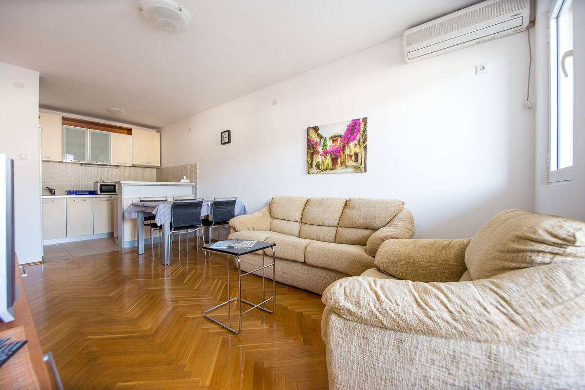 A modern living room with a sofa, a dining table, and a kitchen in the background.