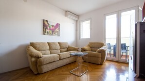 Un salon avec un canapé et un fauteuil, une petite table, un tableau accroché au mur et une porte-fenêtre coulissante donnant sur un espace extérieur.