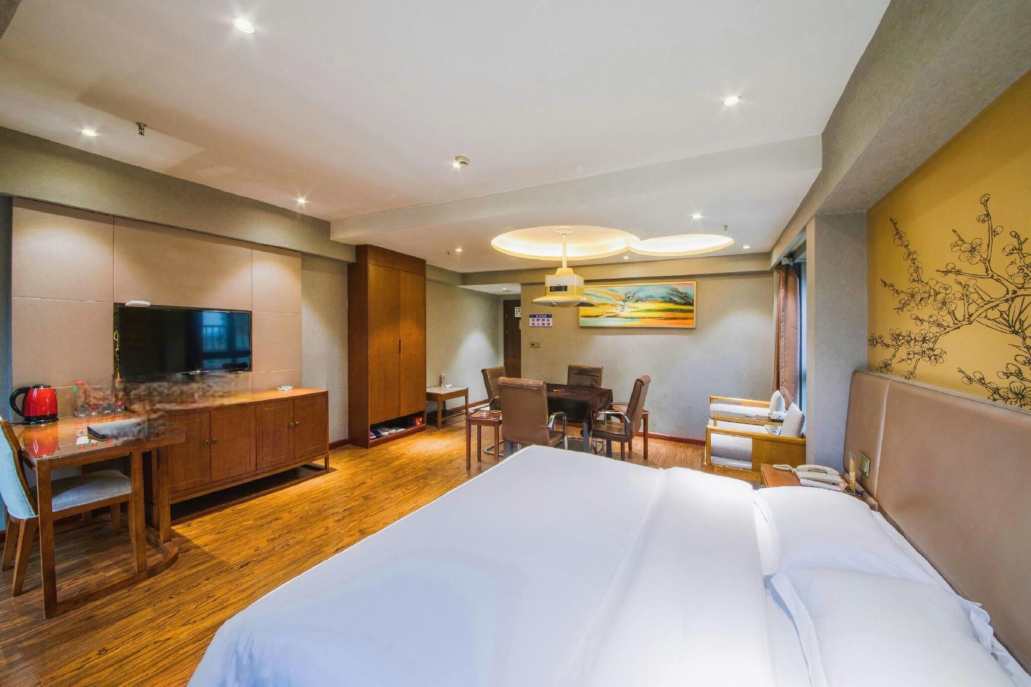 A hotel room with a large bed, a desk with a TV, a dining area, and a painting on the wall.