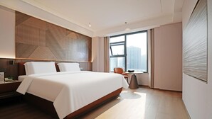 A modern hotel room with a large bed, a wooden accent wall, a view of the city, and a small table with a chair. - Caifu Holiday Hotel (Chongqing)