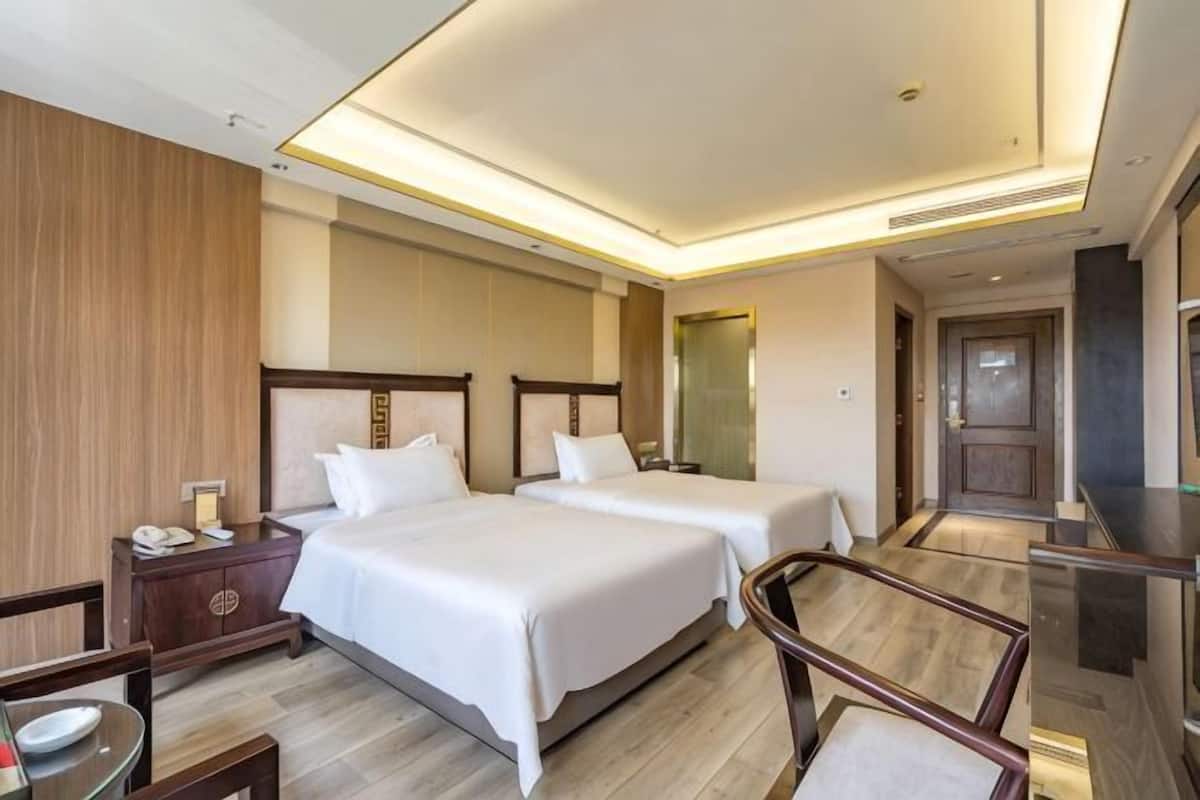 A hotel room with two beds, a desk, a chair, and a television.