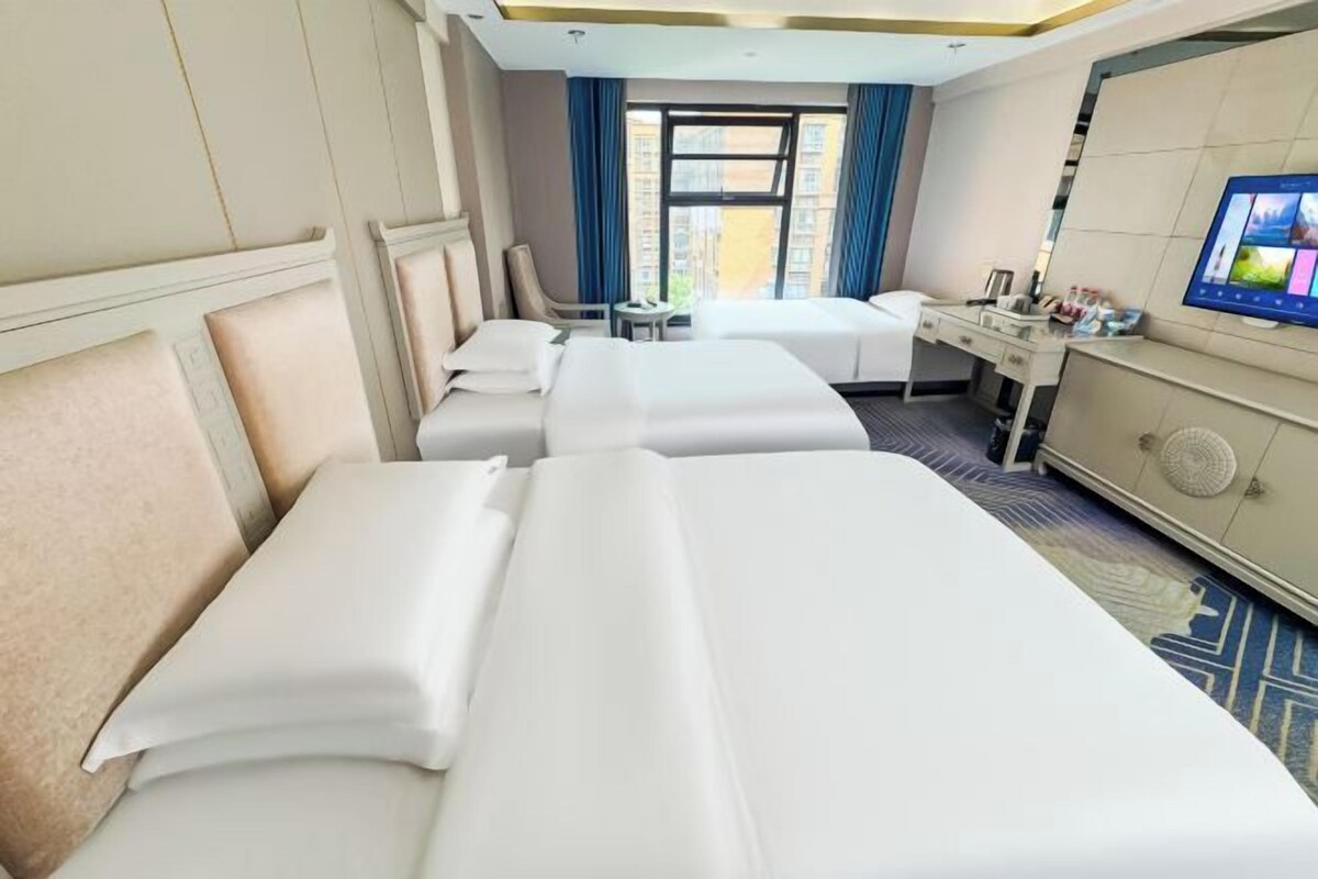 A hotel room with two beds, a desk, a chair, a television, and a window with curtains.