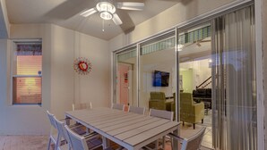 Un comedor con una mesa y sillas, un ventilador de techo y un ventanal corredero que da a una sala de estar.