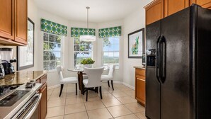 Una cocina moderna con un refrigerador negro, sillas blancas, una mesa de comedor y una cafetera.