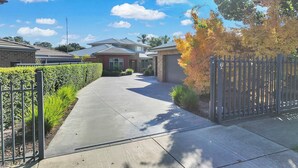 A residential driveway leading to a house with a garage, surrounded by a metal fence and a hedge. - 6A Blair St - Echuca Holiday Homes (Moama)
