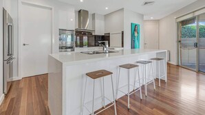 A modern kitchen with a large island, bar stools, and a view of the outdoors. - 6A Blair St - Echuca Holiday Homes (Moama)