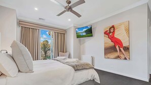 A hotel room with a bed, a ceiling fan, a TV, and a painting. - 6A Blair St - Echuca Holiday Homes (Moama)