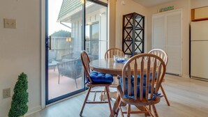 A dining area with a glass door leading to a patio, wooden chairs, a round table, and a decorative black shelf. - Sound side OBX Condo no stairs, pool, enjoy the Fall, less crowds peaceful ! (Kitty Hawk)