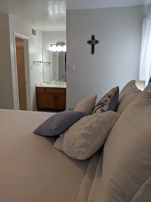 Quarto com uma cama grande, uma cômoda de madeira e um banheiro visível através de uma porta aberta.