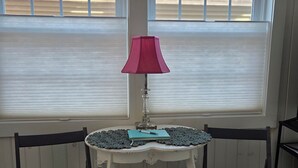 A room with two chairs, a small table with a lamp, and a window with blinds. - Cozy So End Suite (Burlington)
