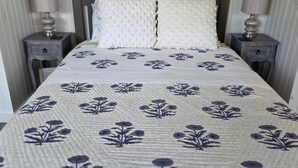 A bed with a floral-patterned quilt, two pillows, and two bedside tables with lamps. - Cozy So End Suite (Burlington)