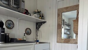 A kitchen with white cabinetry, a stainless steel microwave, a sink with a faucet, and a trash can. - Cozy So End Suite (Burlington)