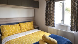 Un dormitorio con cama, ventana con cortinas, radiador y una lámpara en el techo.
